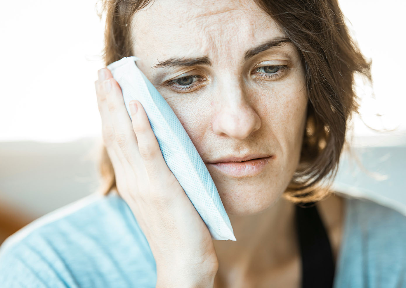 Hygiene & Emergency Care - TD A woman holding an ice pack to her cheek with a pained look on her face